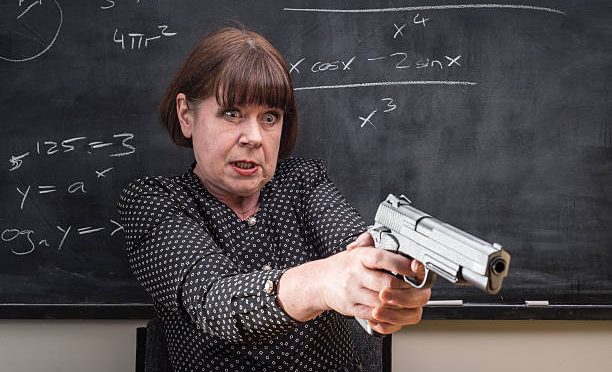 A grumpy older female teacher in front of the classroom